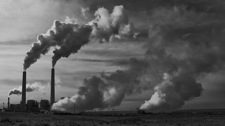 A black and white photo of a power plant emitting pollution.