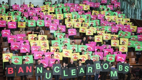 Activists holding up signs spelling out "ban nuclear bombs".