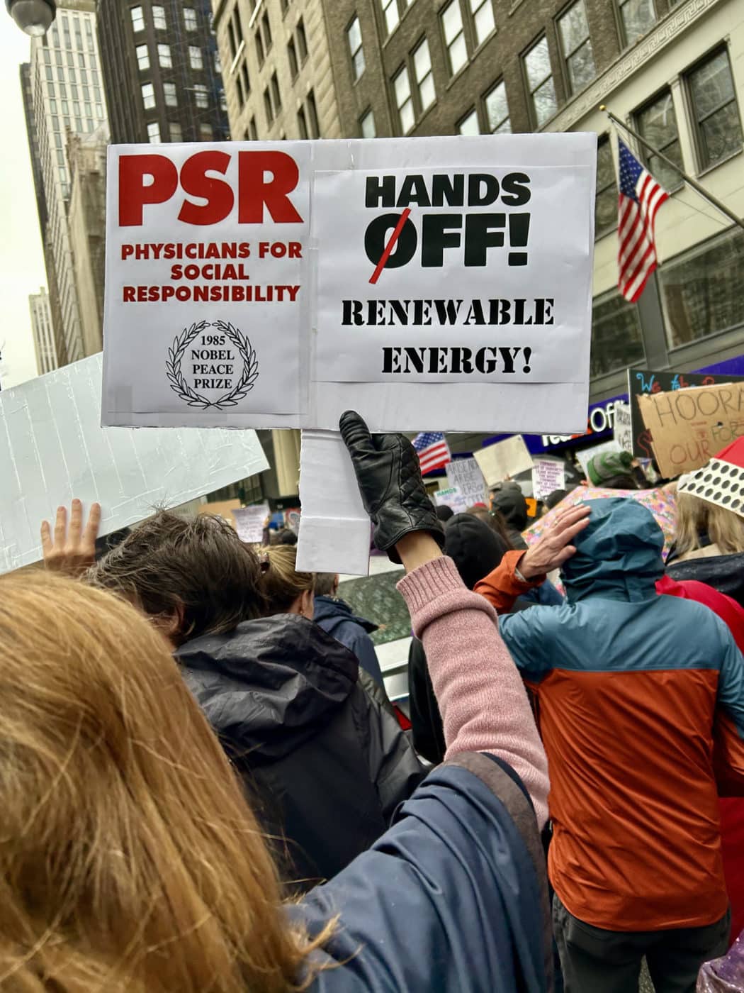 PSR activist holding sign reading "Hands Off Renewable Energy"