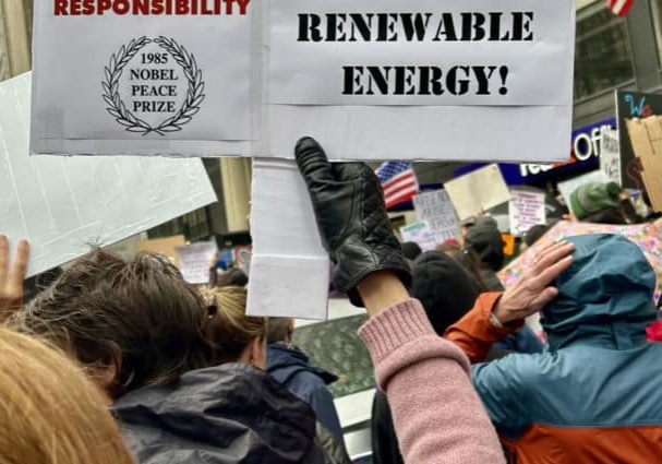 PSR activist holding sign reading "Hands Off Renewable Energy"